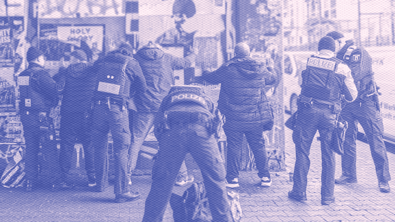 Police carrying out searches on people standing next to a wall